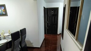 Um corredor com área de refeições, com mesa e cadeiras, um quadro na parede e uma porta no final.