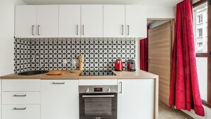 Una cocina compacta con armarios blancos, horno Bosch, salpicadero a blanco y negro y una cortina roja en la ventana.