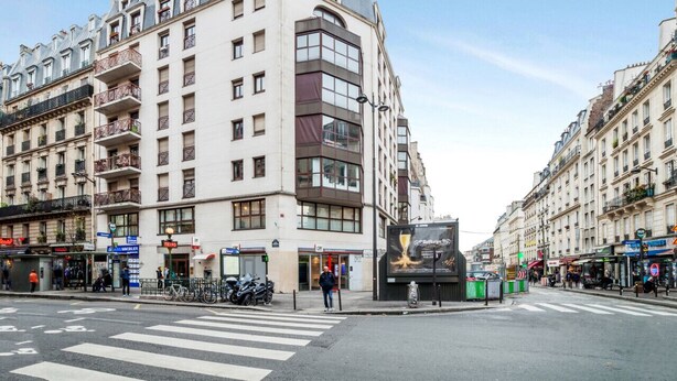 Un edificio de varios pisos con entrada en esquina, un paso de peatones y una calle con bicicletas estacionadas.