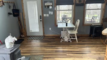 Una habitación acogedora con piso de madera, una mesa con sillas, una ventana con persianas y una puerta con perchero.