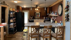 Una cocina con armarios de madera, encimera de mármol y zona de comedor con sillas de madera.