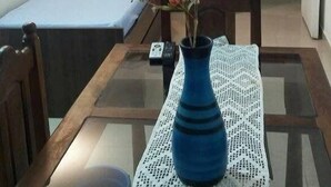 A small room with a dining table, a blue vase with flowers, a TV mounted on the wall, and a bed with a colorful blanket. - Complejo Felesa Las Grutas (Las Grutas)