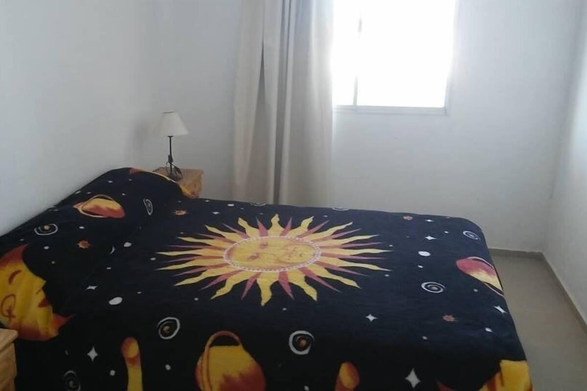 A bedroom with a bed covered in a space-themed bedspread, a bedside lamp, and a window with curtains.