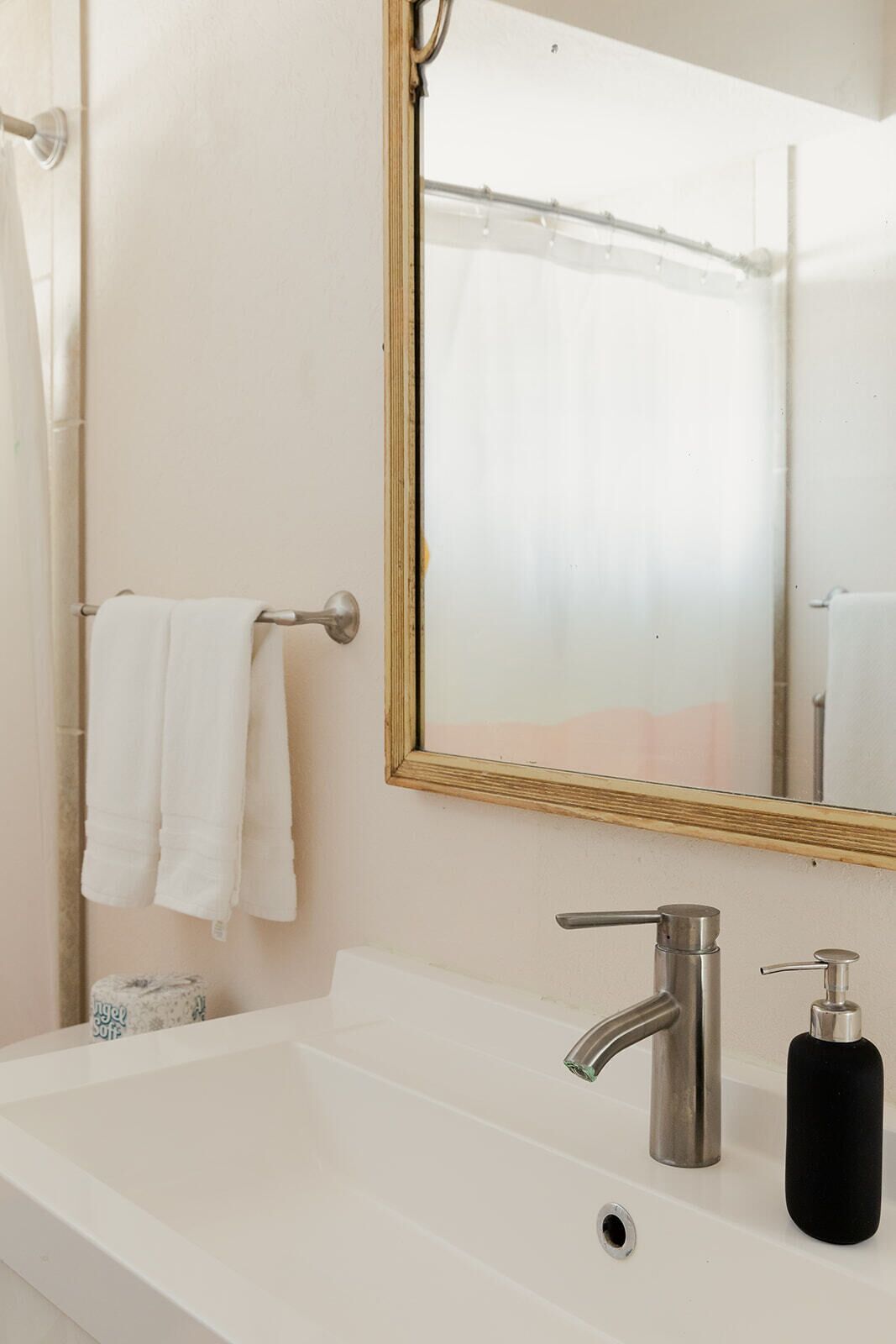 Un baño con un lavabo blanco, un espejo con marco de madera y un perchero con dos toallas blancas.