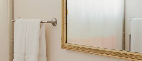 Un baño con un lavabo blanco, un espejo con marco de madera y un perchero con dos toallas blancas.