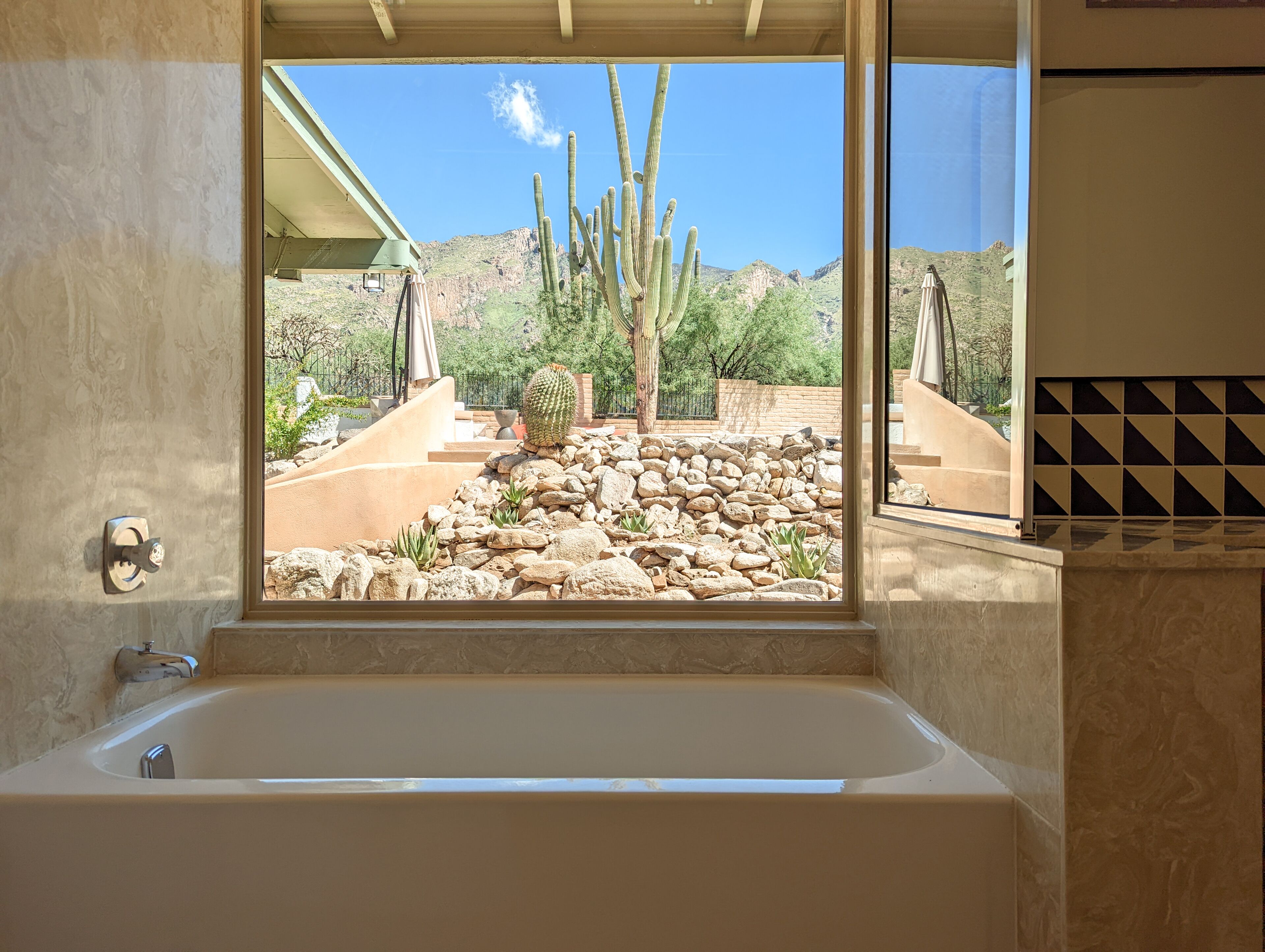Ein Badezimmer mit einer Badewanne und einem Fenster mit Blick auf eine Wüstenlandschaft mit Kakteen und Felsen.