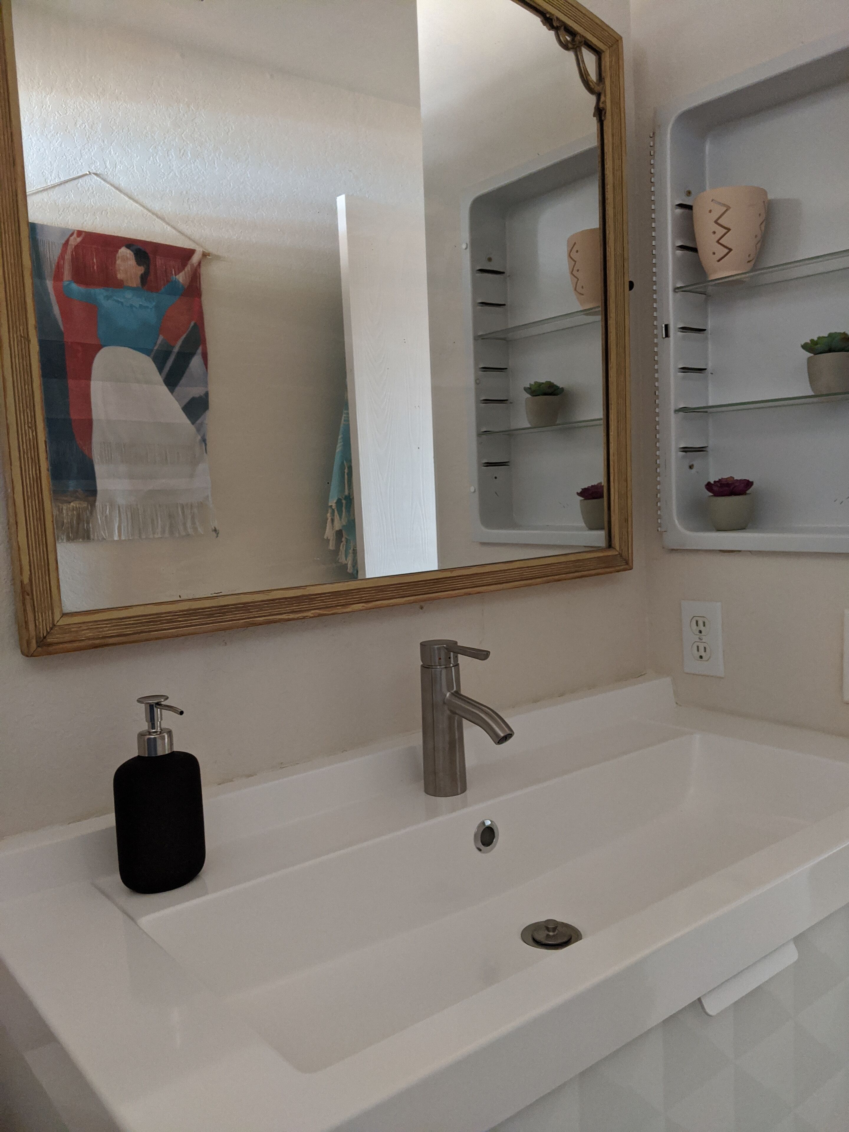 Une salle de bain avec un lavabo blanc, un miroir, une serviette et une étagère ornée d’objets décoratifs.