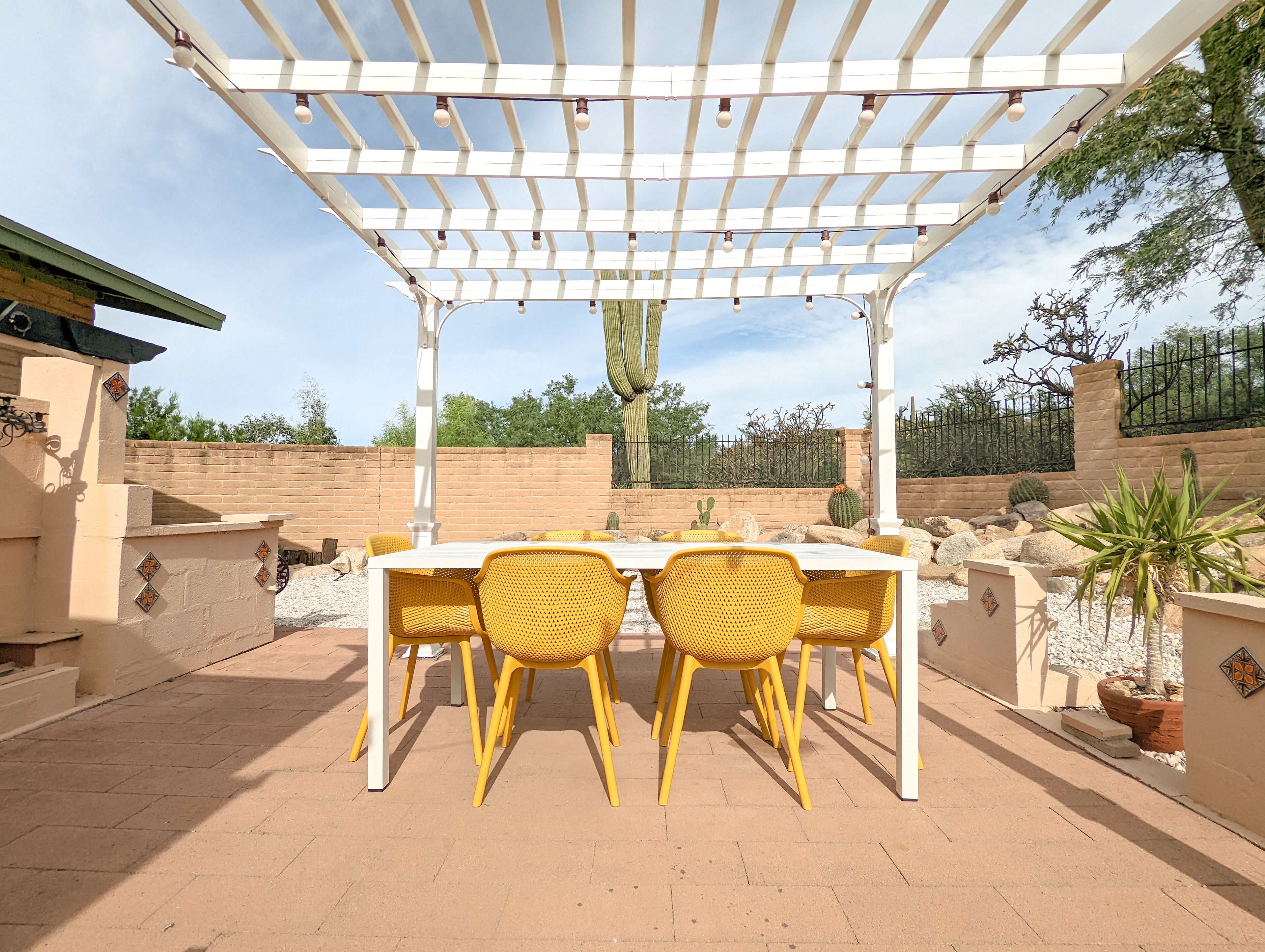 An outdoor patio with a pergola, a table, and yellow chairs.