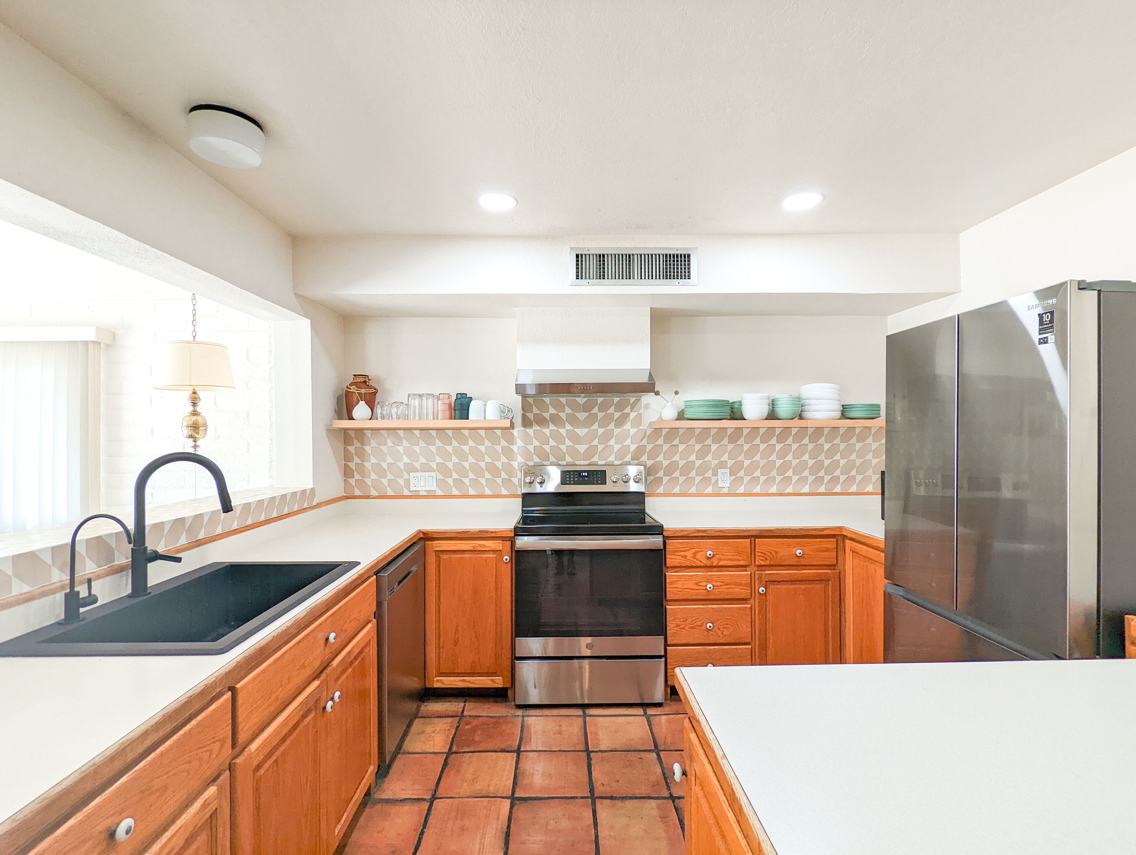 A modern kitchen with wooden cabinets, a stainless steel refrigerator, a built-in oven, and a tiled backsplash.