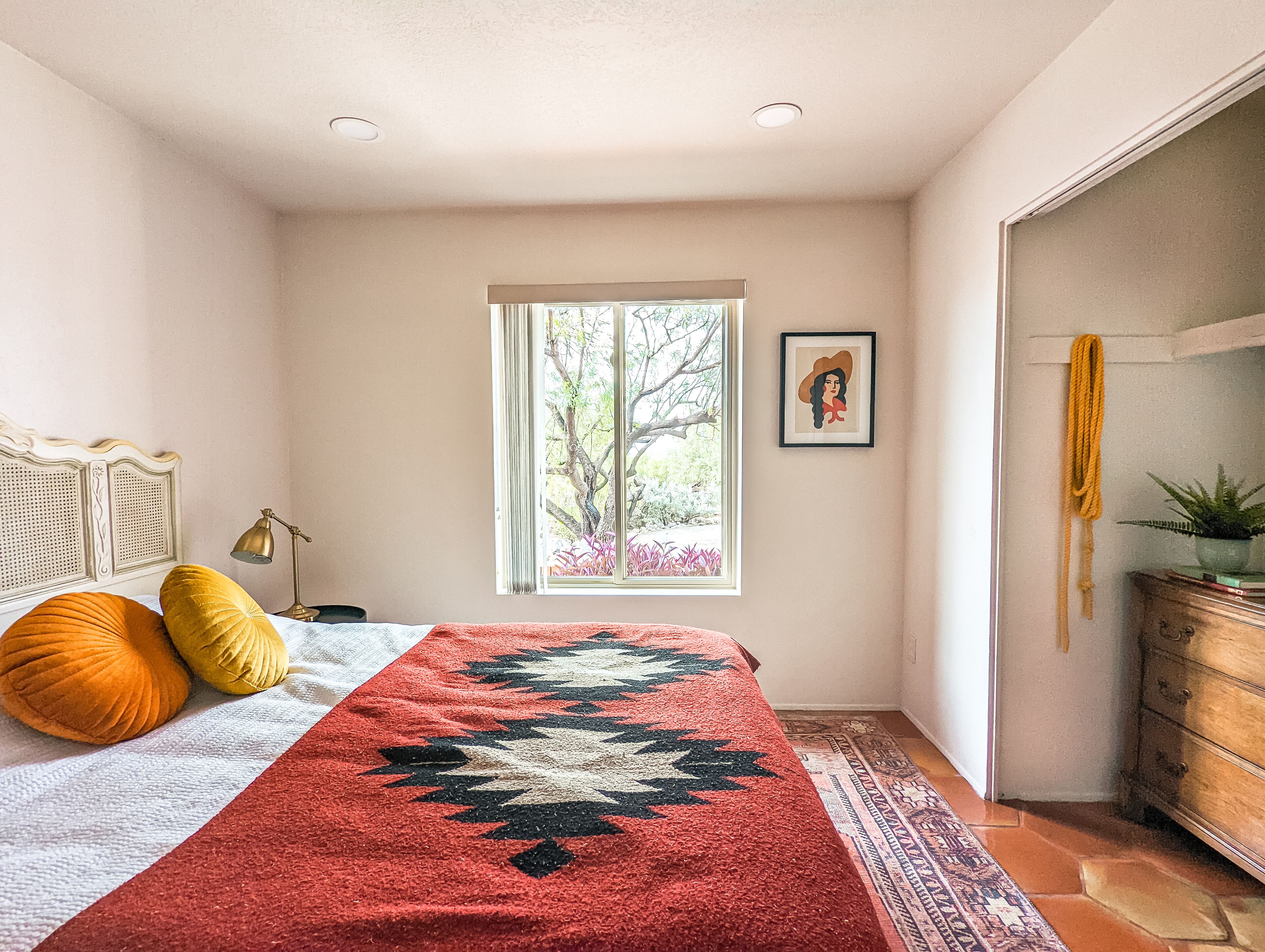 Ein Schlafzimmer mit einem Bett, einem Fenster, einem gerahmten Bild, einer Lampe und einer Kommode.