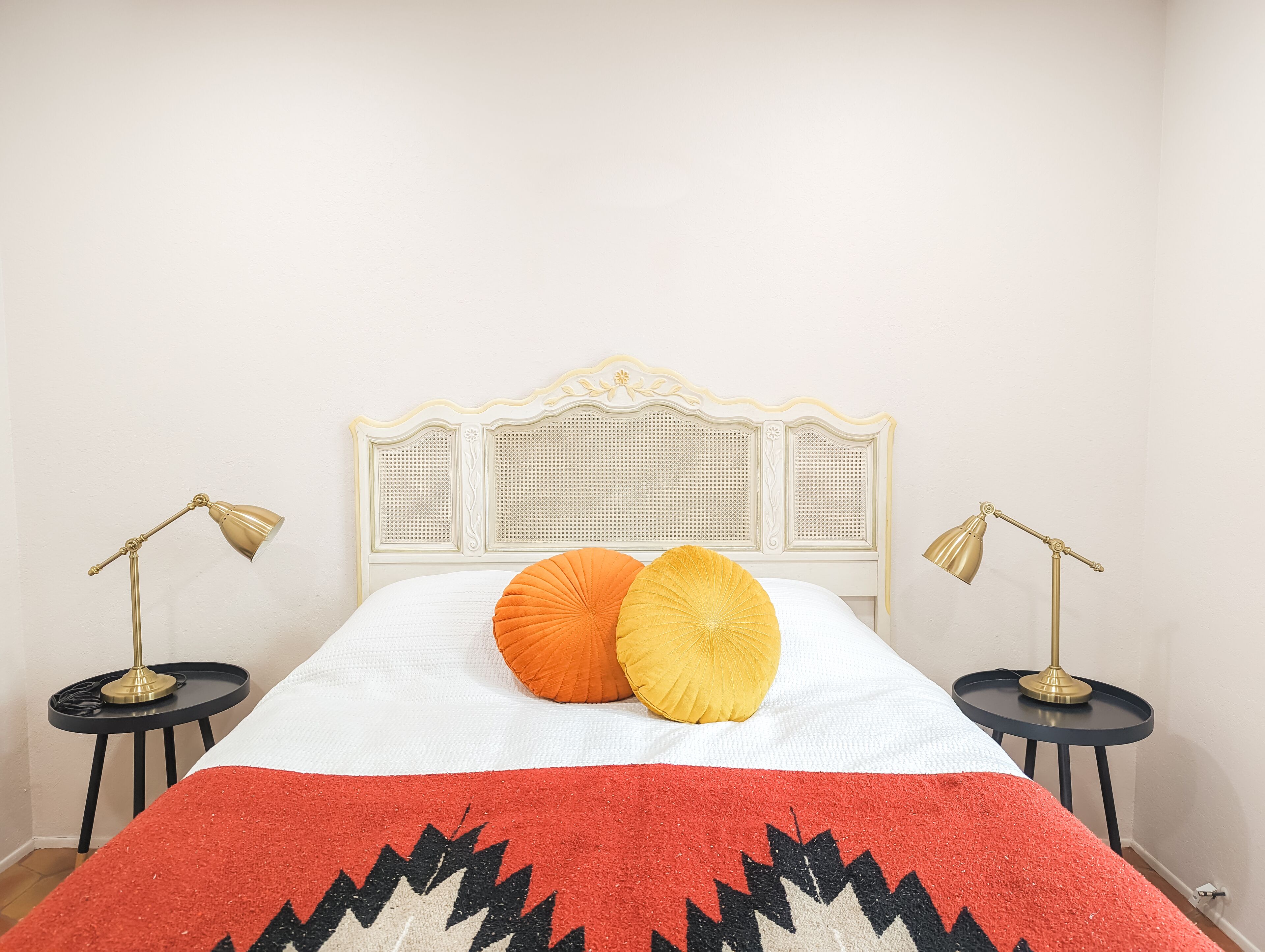Un lit avec une tête de lit blanche, deux lampes de chevet et une couvre-lit à motifs rouges et noirs.