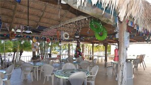 An outdoor dining area with thatched roof, white plastic chairs, and tables. - Life's a beach and Tennis... (Bonita Springs)