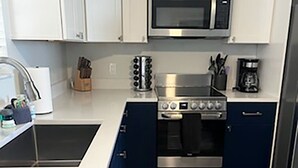 A modern kitchen with white cabinets, a stainless steel microwave, a stove, and a coffee maker. - Life's a beach and Tennis... (Bonita Springs)