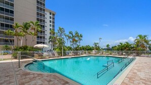 A swimming pool with a curved edge, surrounded by palm trees and lounge chairs, with a high-rise building in the background. - Life's a beach and Tennis... (Bonita Springs)