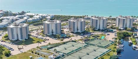 Ett bostadsområde vid kusten med höga byggnader, en parkeringsplats och en tennisbana.