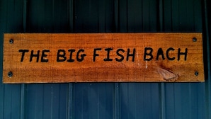 Ein Holzschild mit der Aufschrift 'THE BIG FISH BACH' an einem wellenförmigen Metalluntergrund.