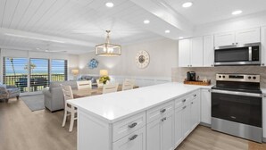 Une cuisine moderne avec des meubles blancs, un îlot central, un four encastré et un four à micro-ondes.