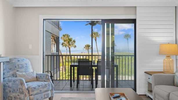 Une chambre avec vue sur l’océan, un balcon avec une table et des chaises, un canapé et une lampe.