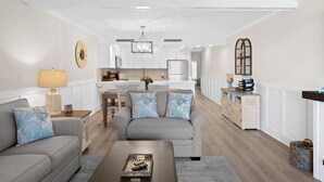 Un salon moderne avec un canapé, une table basse et un coin repas, la cuisine étant visible au fond.