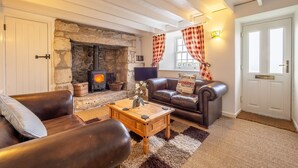A cozy living room with a stone fireplace, leather sofas, a wooden coffee table, and a checkered curtain. - A beautiful, dog-friendly holiday home with magnificent views of two coastlines (Praa Sands)