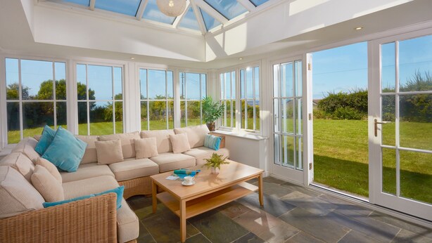 A sunlit room with a large glass door leading to a garden, a beige sofa, and a wooden coffee table. - A beautiful, dog-friendly holiday home with magnificent views of two coastlines (Praa Sands)