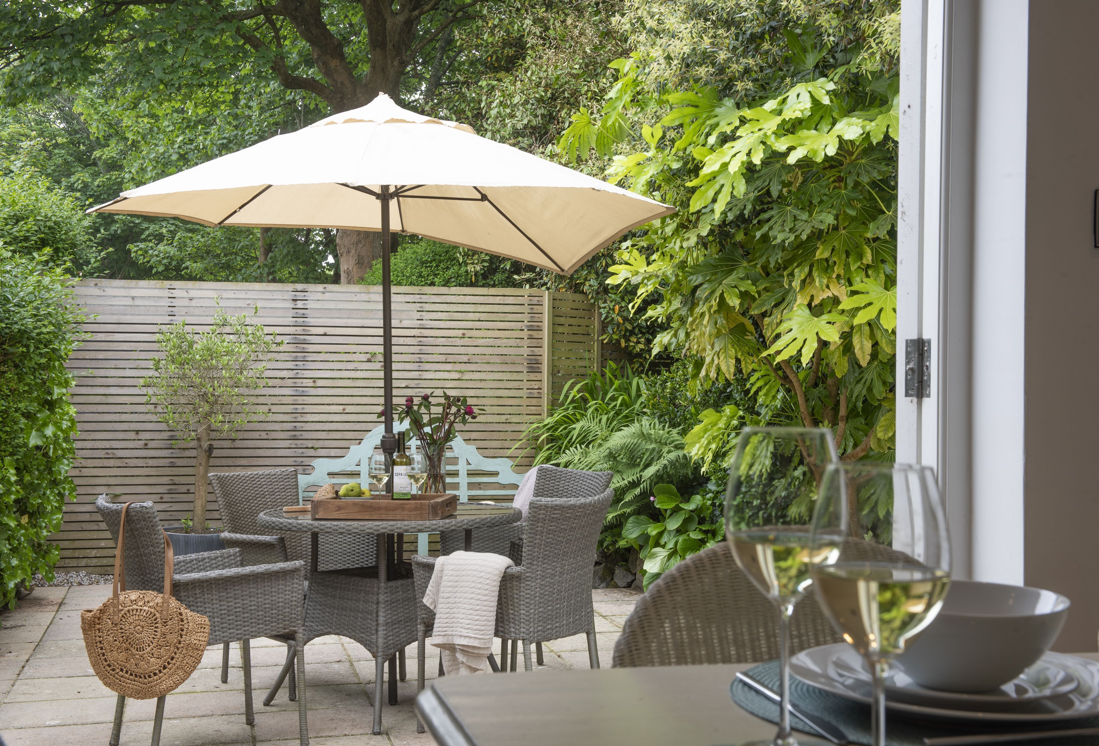Eine Terrasse im Freien mit Korbmöbeln, einem Tisch und einem großen Sonnenschirm.