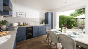 Una cocina moderna con armarios azules, un comedor con mesa y sillas blancas, y vista a zonas verdes.