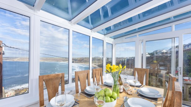 A dining area with a table set for four, large windows, and a view of the ocean. - This property combines a breath-taking coastal location with modern styling (Sennen Cove)