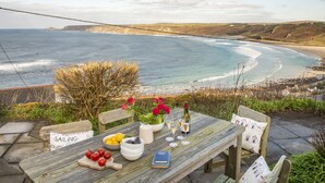 A wooden table with a view of the ocean, a bottle of wine, and a book. - This property combines a breath-taking coastal location with modern styling (Sennen Cove)