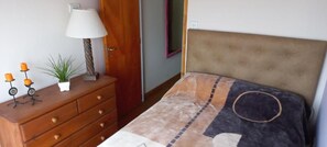 A bedroom with a bed, a dresser, a lamp, and a small plant. - La casa de Titi (Querétaro)