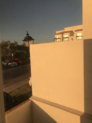 A view from a balcony overlooking a street with parked cars and a building with a white facade and tiled roof. - La casa de Titi (Querétaro)