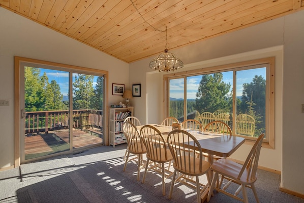 Enjoy meals in a dining area with a table and chairs, surrounded by windows offering a view of the deck and forest.