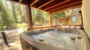 A hot tub on a wooden deck with a view of a forest and a building in the background.