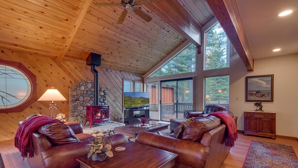 A cozy living room with a stone fireplace, leather sofas, a wooden coffee table, and a large window offering a view of the outdoors.