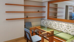 Une pièce comprenant une table à manger avec un plateau en verre, une chaise rembourrée de tissu bleu, un banc en bois avec un revêtement à motifs floraux et des étagères en bois ornées de petites plantes.