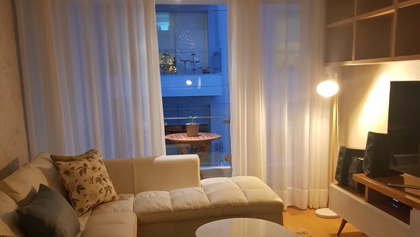 Un salon avec un canapé, une table basse et un meuble pour la télévision. On aperçoit un balcon avec une table et des chaises à travers la fenêtre.