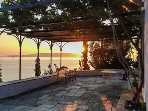 En terrasse med flisebelægning, et pergola og havudsigt i solnedgangen.
