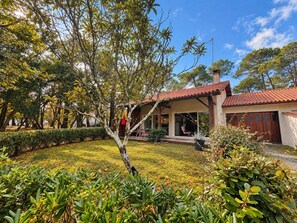 Ein Haus mit überdachter Terrasse, umgeben von gepflegten Gärten und Bäumen.