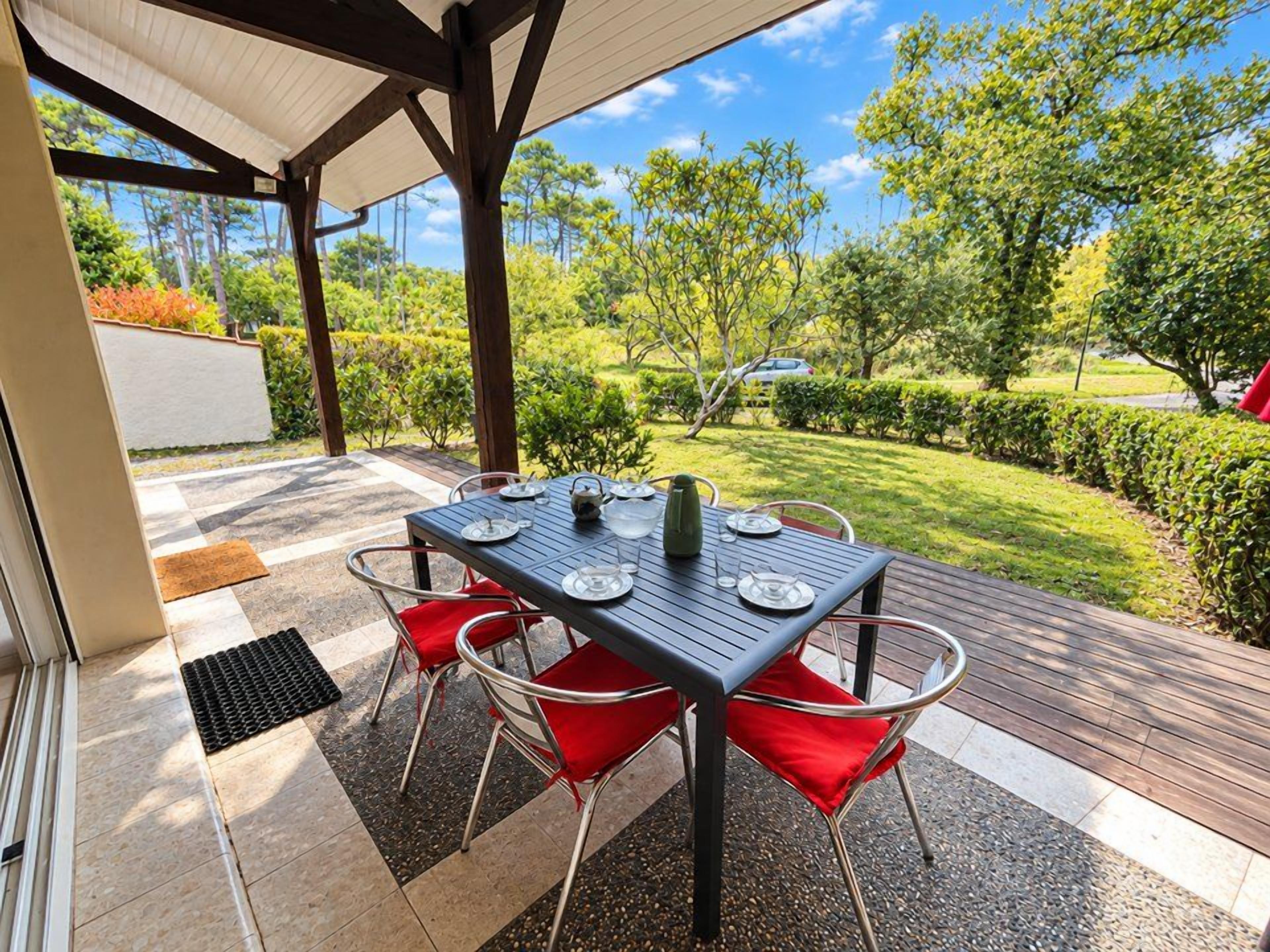 An outdoor patio with a table set for dining, surrounded by chairs, and a view of a landscaped garden.