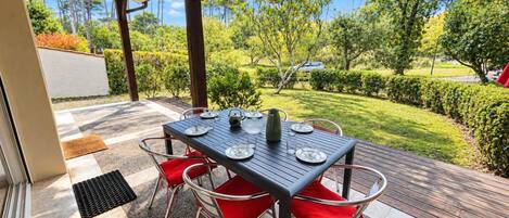 An outdoor patio with a table set for dining, surrounded by chairs, and a view of a landscaped garden.