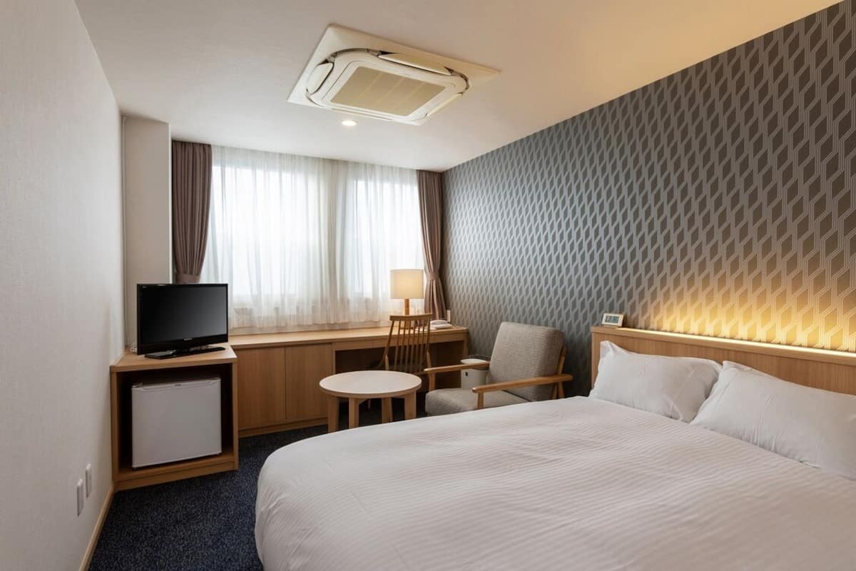 A hotel room with a bed, a desk with a computer, a television, and a small refrigerator.