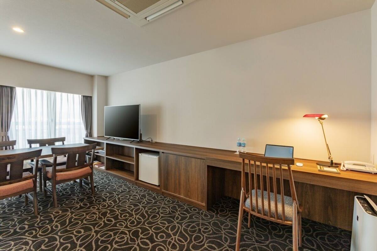 A hotel room with a desk, chair, television, and a small refrigerator.