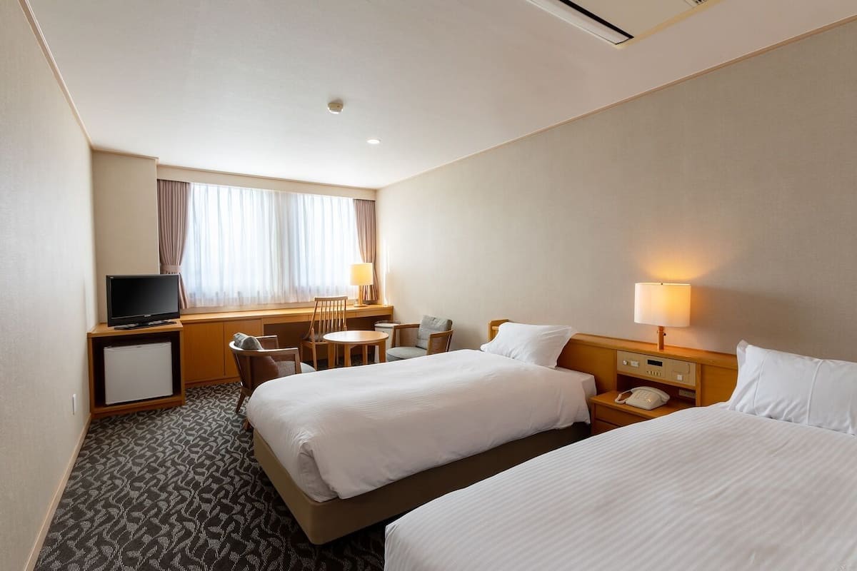 A hotel room with two beds, a desk with a television, a small table, and a chair.