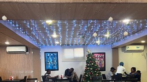 A restaurant with wooden panel ceilings, tables, chairs, and a decorated Christmas tree. - Diana Hotel (Monrovia)