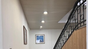 A hallway with a wooden staircase, white walls, and a framed picture on the wall. - Diana Hotel (Monrovia)