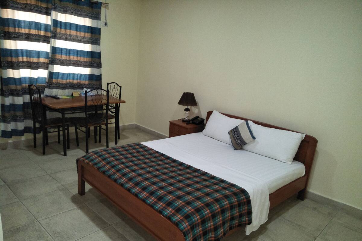 A bedroom with a bed, a bedside table with a lamp, a chair, and a small table.