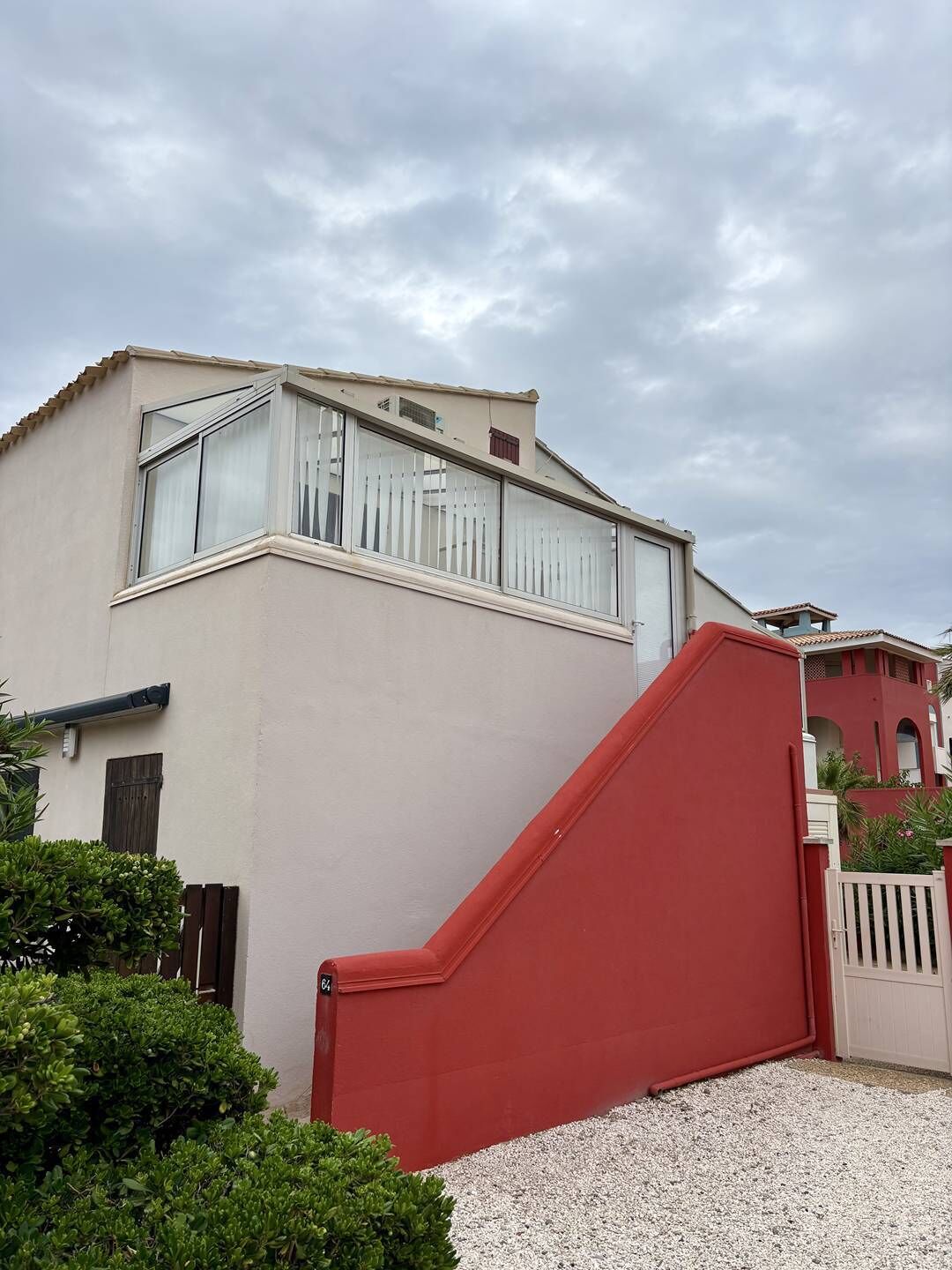 Un bâtiment à la façade beige, doté d’un portail rouge et d’une clôture blanche.
