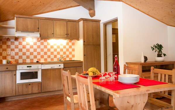 Une cuisine avec des meubles de rangement en bois, un dosseret à carreaux, une table à manger avec des chaises et une plante en pot.