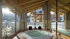 Area benessere con vasca idromassaggio, ampie finestre e vista su una montagna.