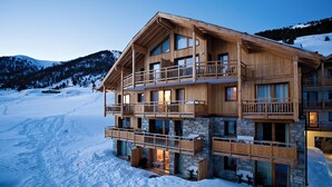 Un lodge in legno a più piani con balconi, livelli inferiori in pietra e uno sfondo montuoso innevato.